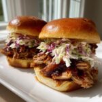 Two appetizing smoked pulled pork sliders piled high with barbecue sauce and creamy coleslaw on brioche buns.