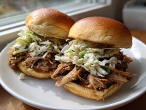Two perfect smoked pulled pork sliders piled high with creamy coleslaw, served on a white plate.