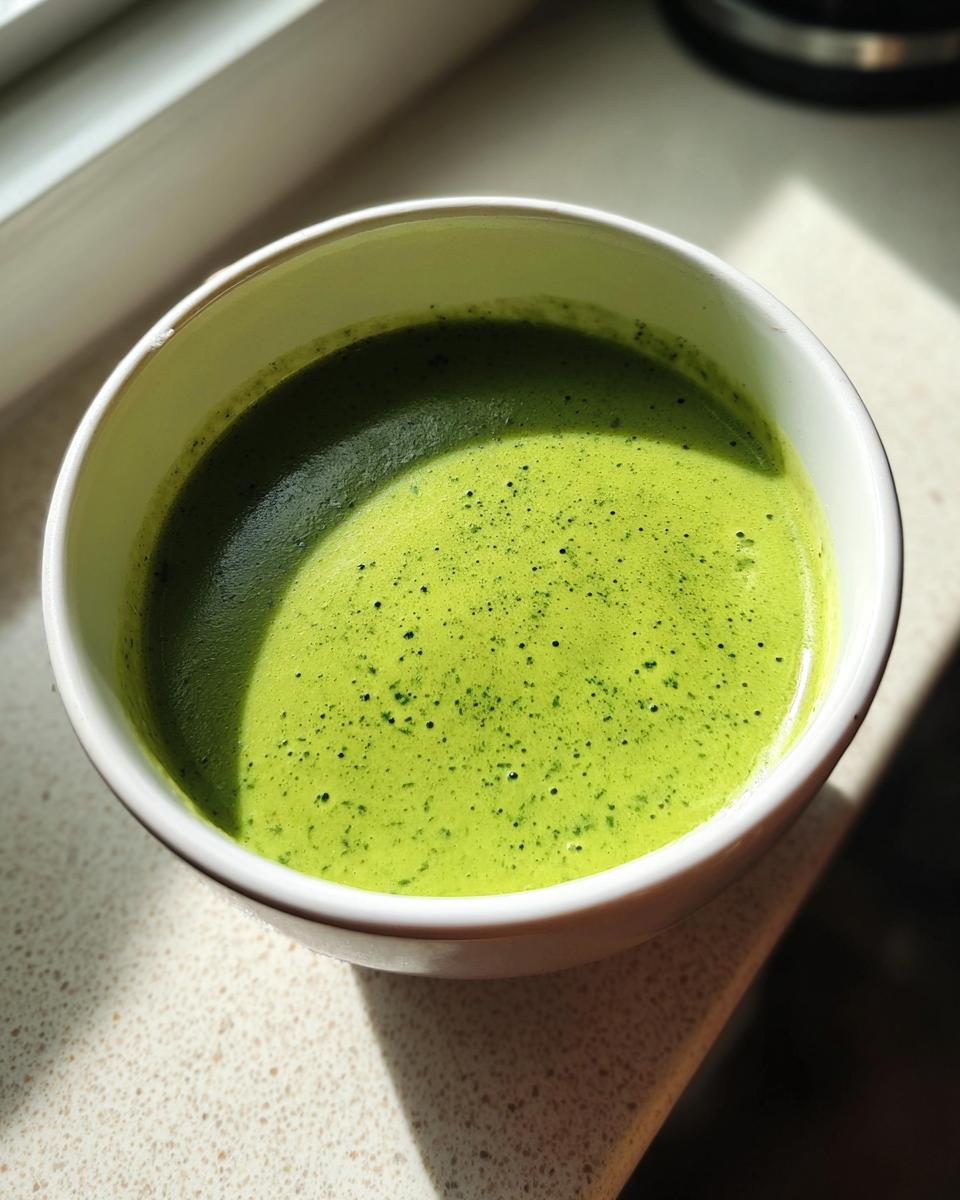 Close-up of a vibrant green bowl of creamy spring pea soup, highlighted by sunlight.
