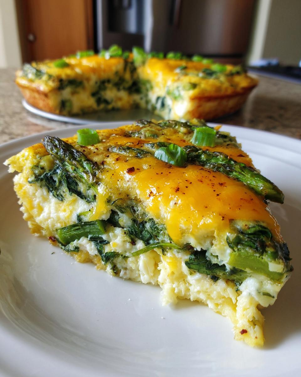 A close-up slice of Spring veggie egg bake featuring spinach, asparagus, and melted cheddar cheese on a white plate.