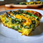 A close-up slice of a bright yellow Spring veggie egg bake topped with bright green asparagus spears and melted cheese.
