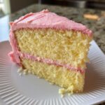 Close-up of a moist slice of Strawberry Lemonade Cake showing two layers of yellow cake and pink strawberry frosting.