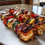 Close-up of perfectly cooked grilled chicken kabobs featuring glazed chicken, zucchini, red bell pepper, and red onion.