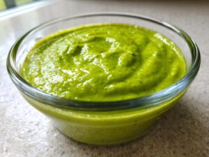 Close-up of thick, vibrant green Spring pea soup swirled in a clear glass bowl.
