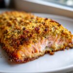 Close-up of a perfectly cooked Walnut crusted salmon fillet with a golden brown, crunchy topping on a white plate.